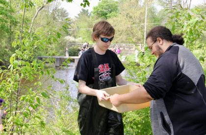 Two Albion College community members working outside by a river holding a tub of water
