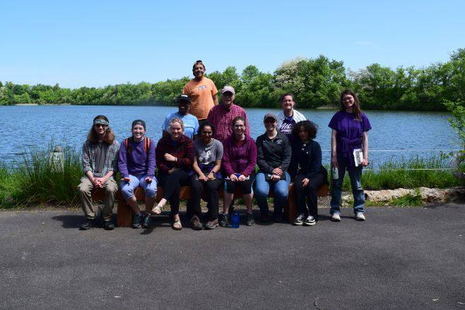 Group of students and faculty outside in front of a blue body of water.