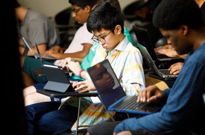 Students working on laptop computers in a classroom setting.