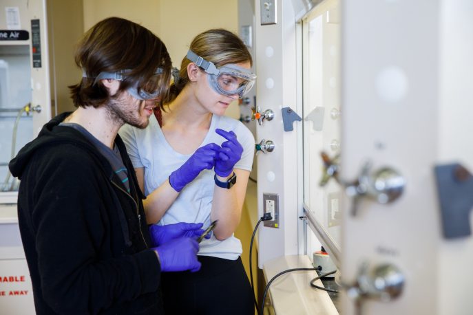 Two students wearing protective goggles in a lab setting.