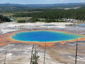 Deep blue naturally occurring spring in the ground with trees and hills in the background.