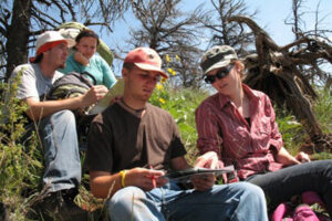 Four students sitting in the grass on a hill.