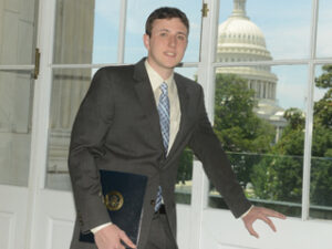 A student in a suit standing in front of a window.