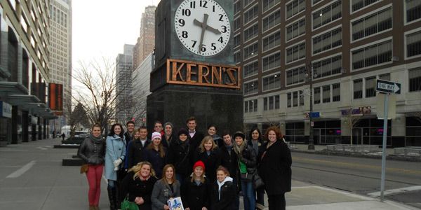 A group of students wearing coats standing in front of a giant clock that says 