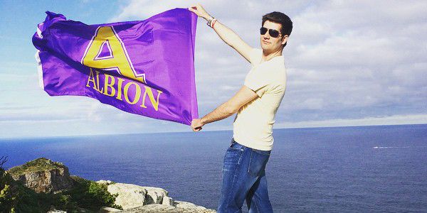 A student standing in front of the ocean holding an Albion flag.