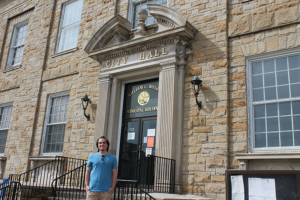 A photograph of a student standing in front of a stone City Hall building.