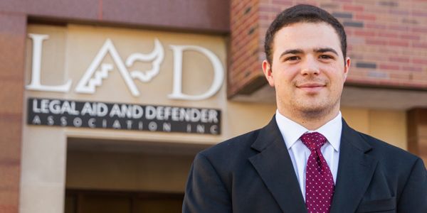 A student in a suit standing in front of a building.