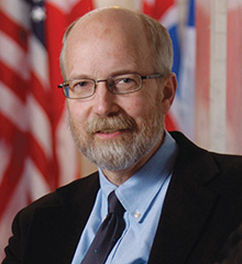 A headshot of a man in front of a flag.
