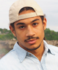 A headshot of a student wearing a backwards baseball cap and a white shirt.