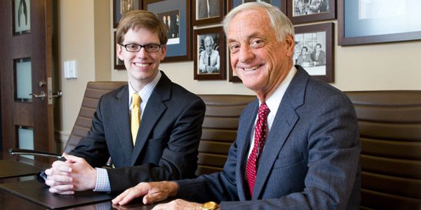 A student sitting next to a man. Both are wearing suits.