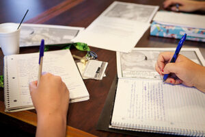 Open notebooks with hands holding pens to the paper as if to write in them.