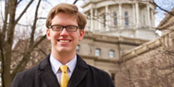 A student standing in front of a building and a tree.
