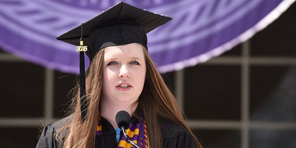 A student in cap and gown speaking into a microphone.