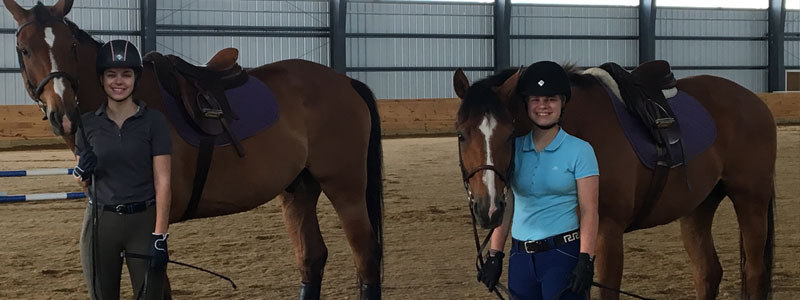 Two women standing next to their horses