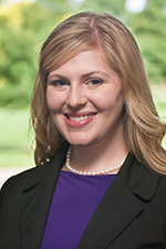 A person in a purple shirt wearing a pearl necklace.
