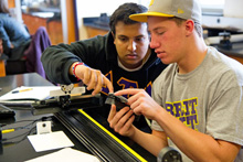 Two students looking intently at a part as they work on a research project.