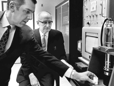 E.T.S. Walton watches as another man places a small white cylinder into a machine.