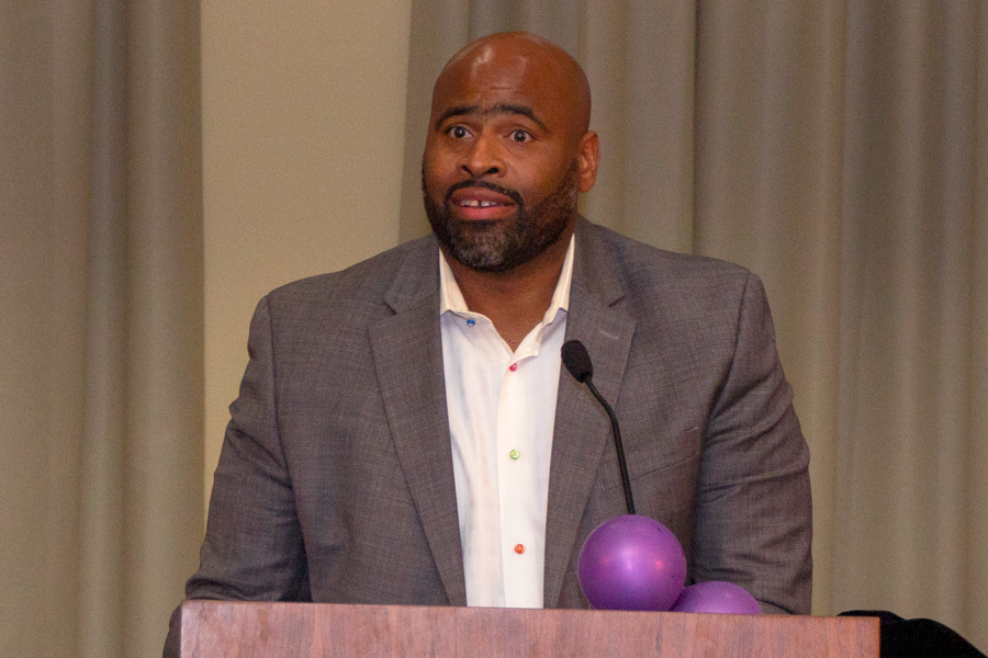 Pastor Leon McDonald wearing a coat and a white shirt with colored buttons, addresses students for his alumni address.